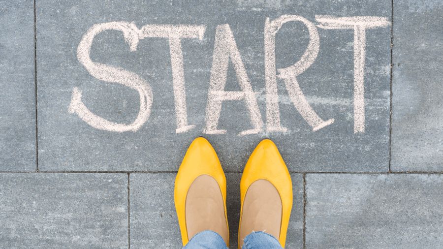 Feet in yellow shoes stand on pavement with "START" written in chalk.