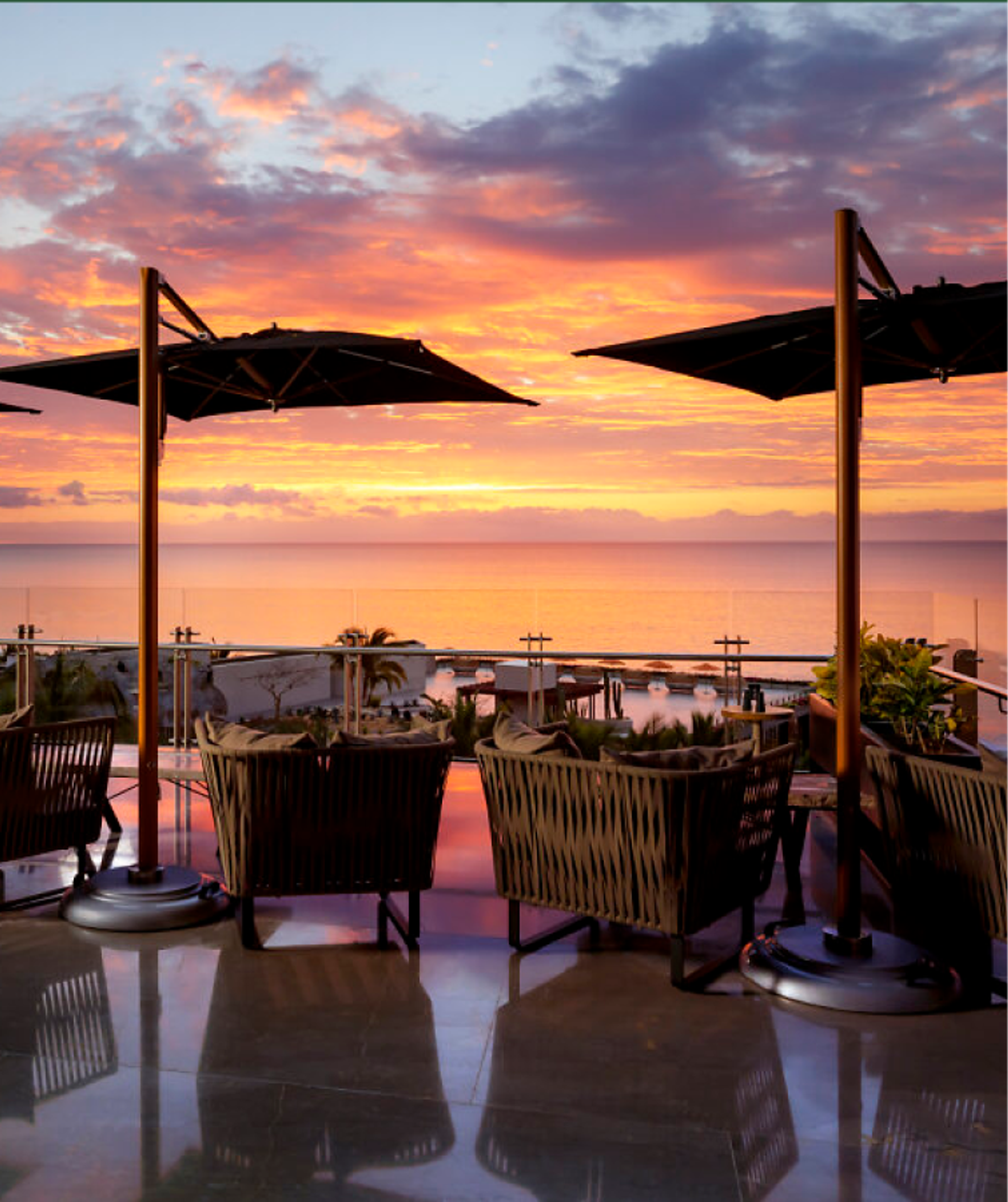 Patio with umbrellas and chairs overlooking a vibrant sunset over the ocean.