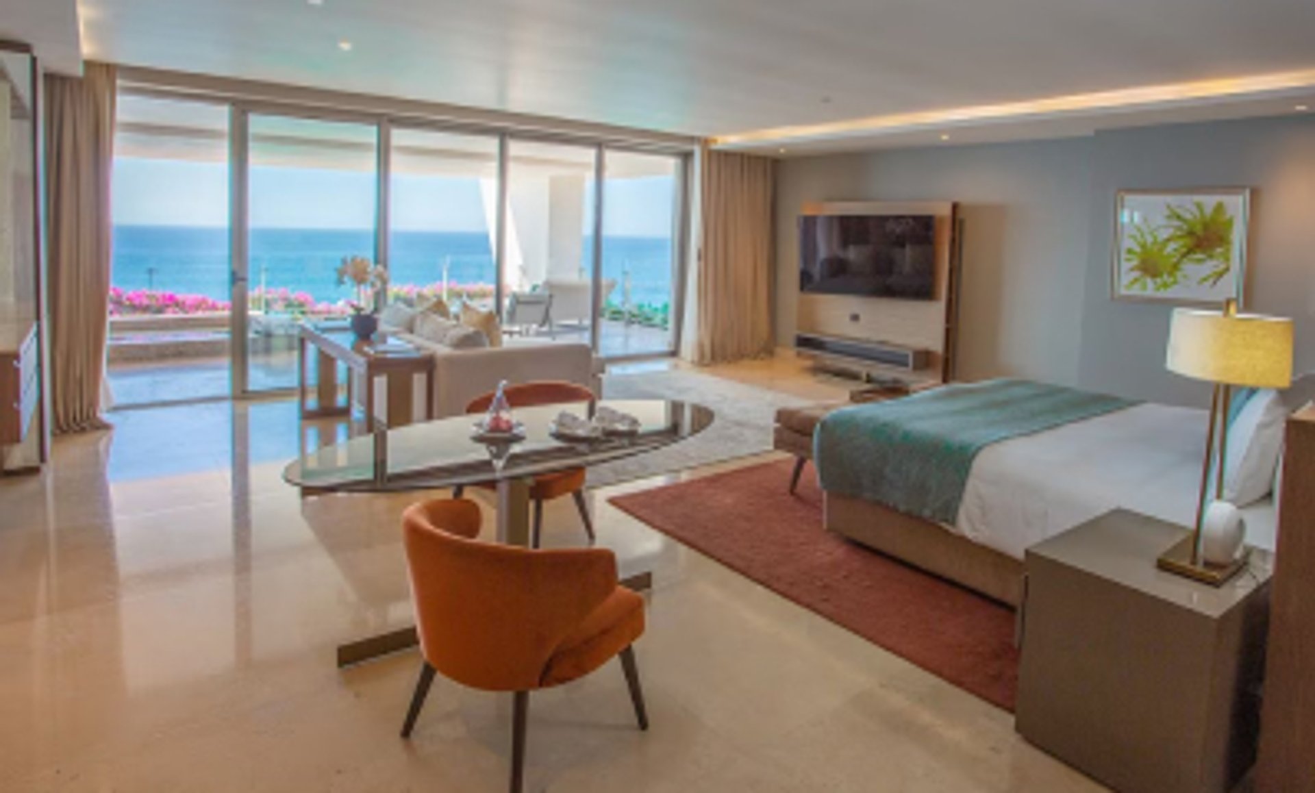 A modern suite with a bed, dining area, and living space, featuring a large balcony with an ocean view.