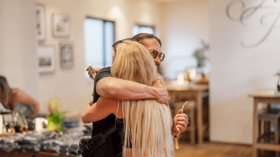 A man with glasses smiling while hugging a woman with long blonde hair.