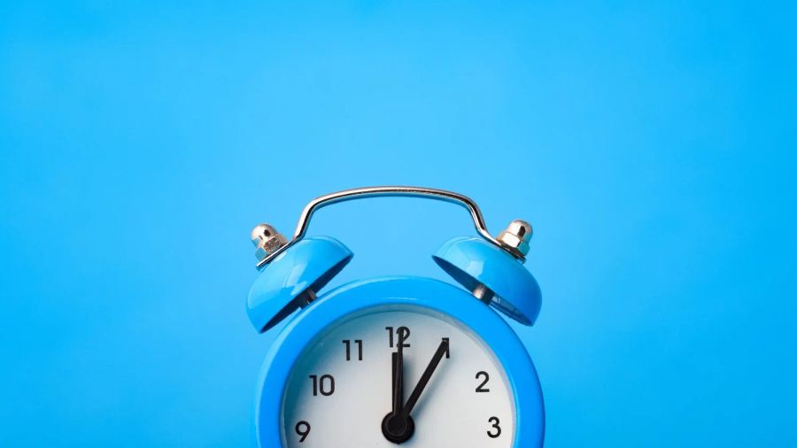 Blue alarm clock set to 1 o'clock against a blue background.