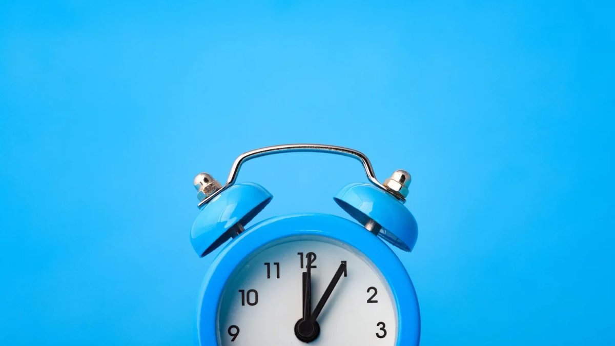 Blue alarm clock set to 1 o'clock against a blue background.