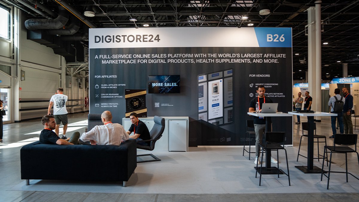 Digistore24 booth B26 at a trade show, featuring a large banner advertising its online sales platform, with several people gathered and interacting.