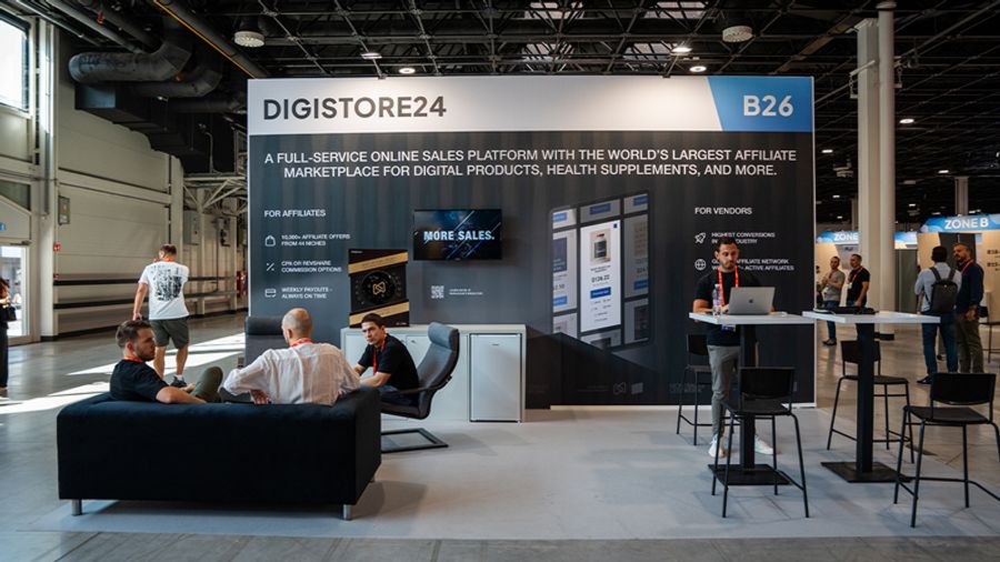 Digistore24 booth B26 at a trade show, featuring a large banner advertising its online sales platform, with several people gathered and interacting.