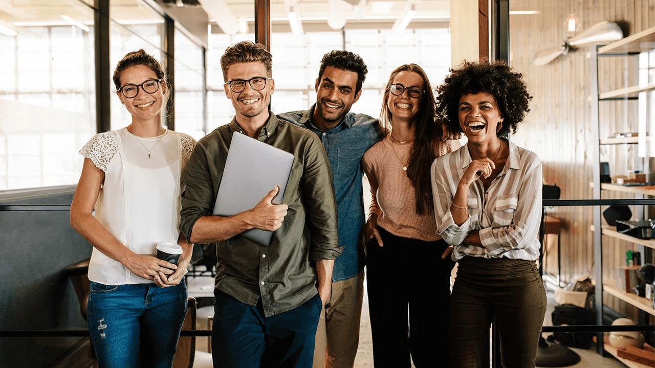 A diverse group of five smiling colleagues standing in an office.