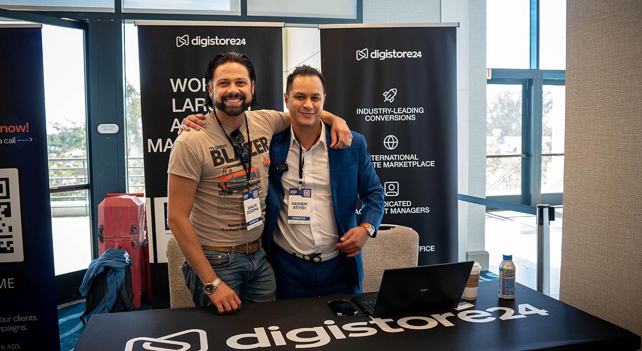 Two smiling men pose at a Digistore24 booth during an event.