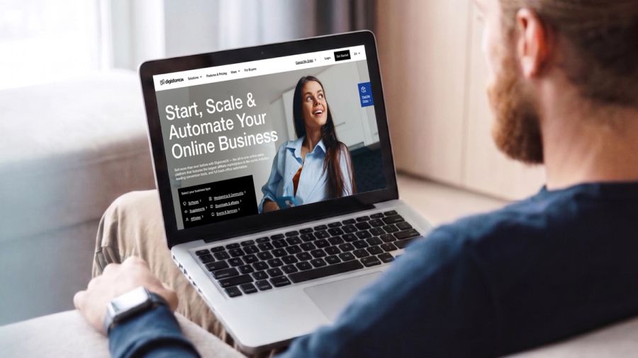 Bearded man views a laptop screen displaying a website for online business automation, featuring a smiling woman.