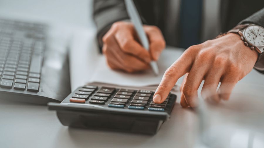 Hands using a calculator and writing, with a laptop nearby.