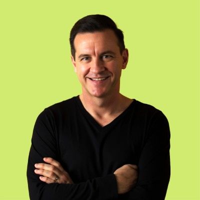 Smiling man in a black V-neck shirt with crossed arms against a lime green background.