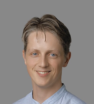 Headshot of a smiling man with short blonde hair and blue eyes in a light blue shirt.