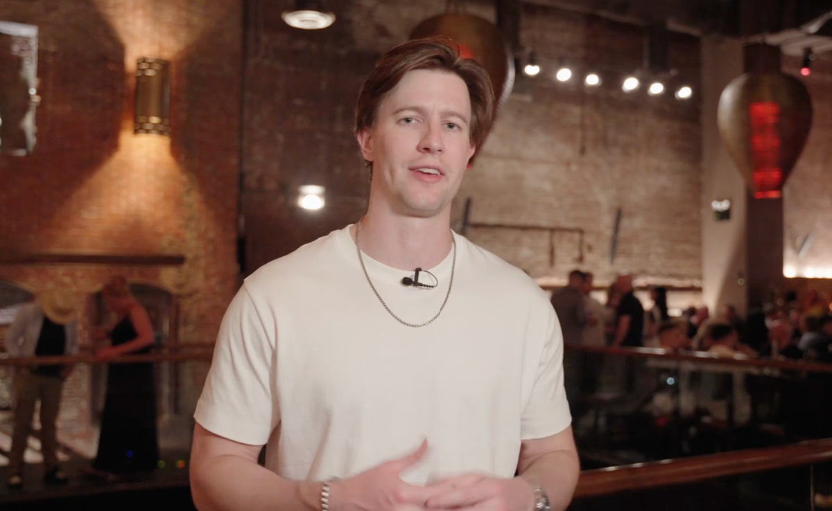 A man wearing a lavalier microphone speaks in a dimly lit, bustling restaurant.