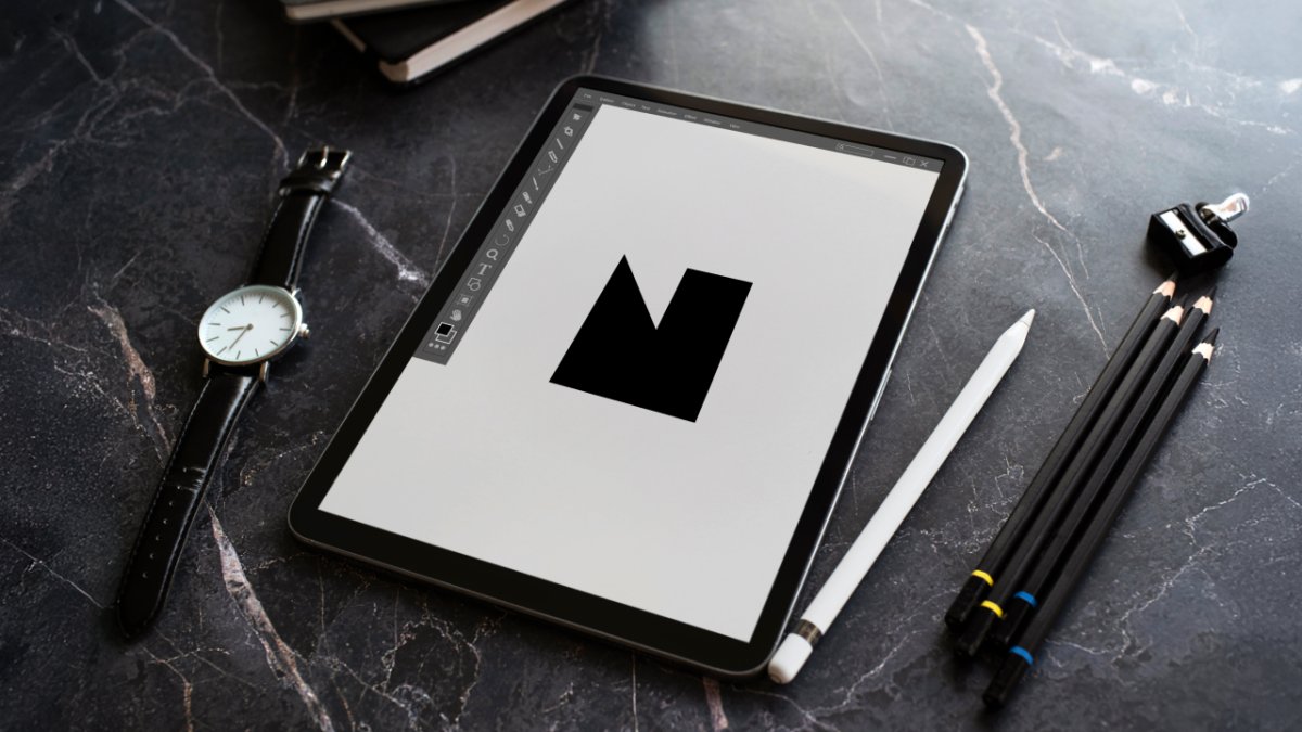 Tablet displaying a black 'M' design, Apple Pencil, watch, and pencils on a dark marble desk.