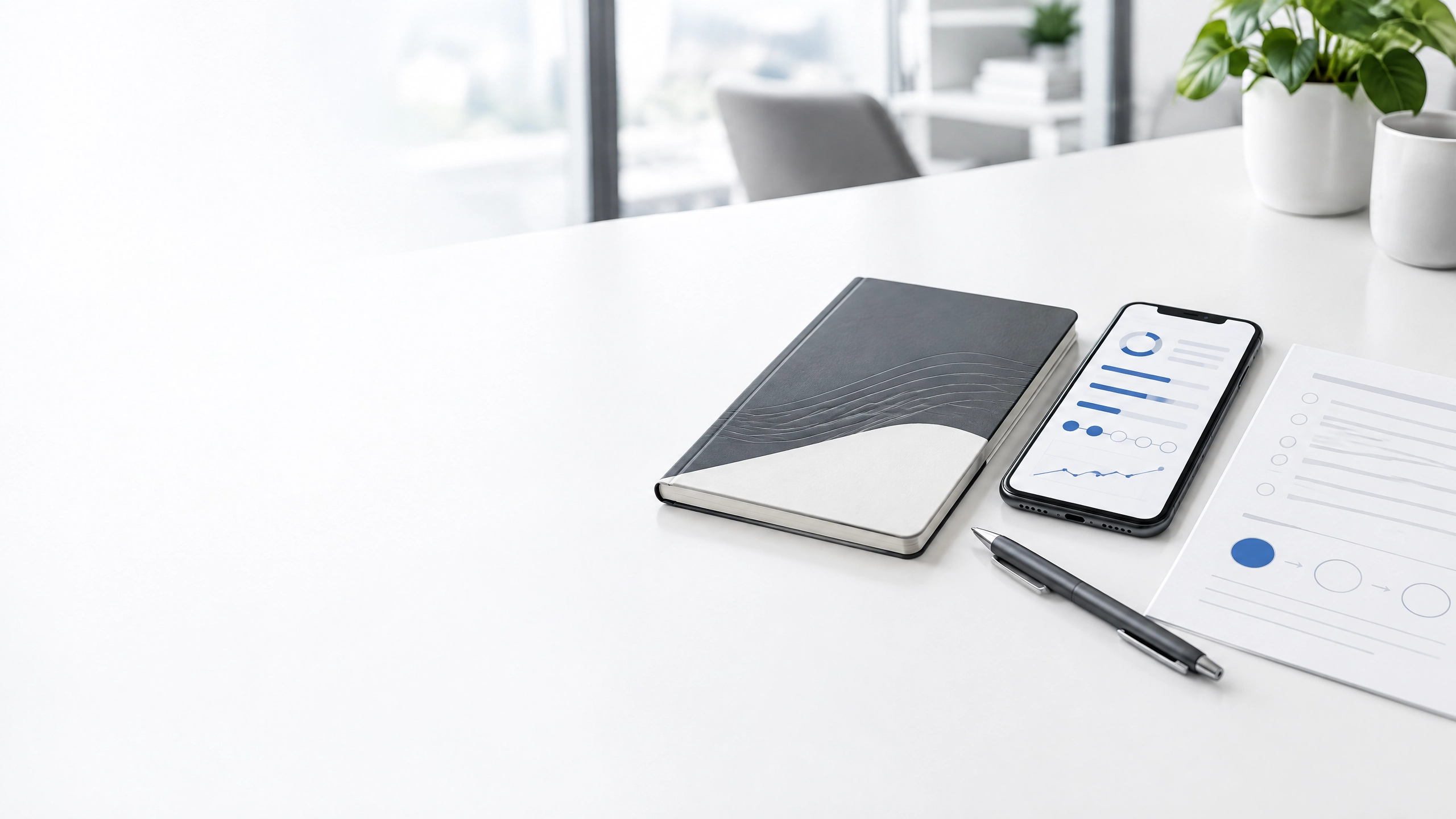 A white desk with a notebook, and a smartphone displaying data charts, a pen, and a document.