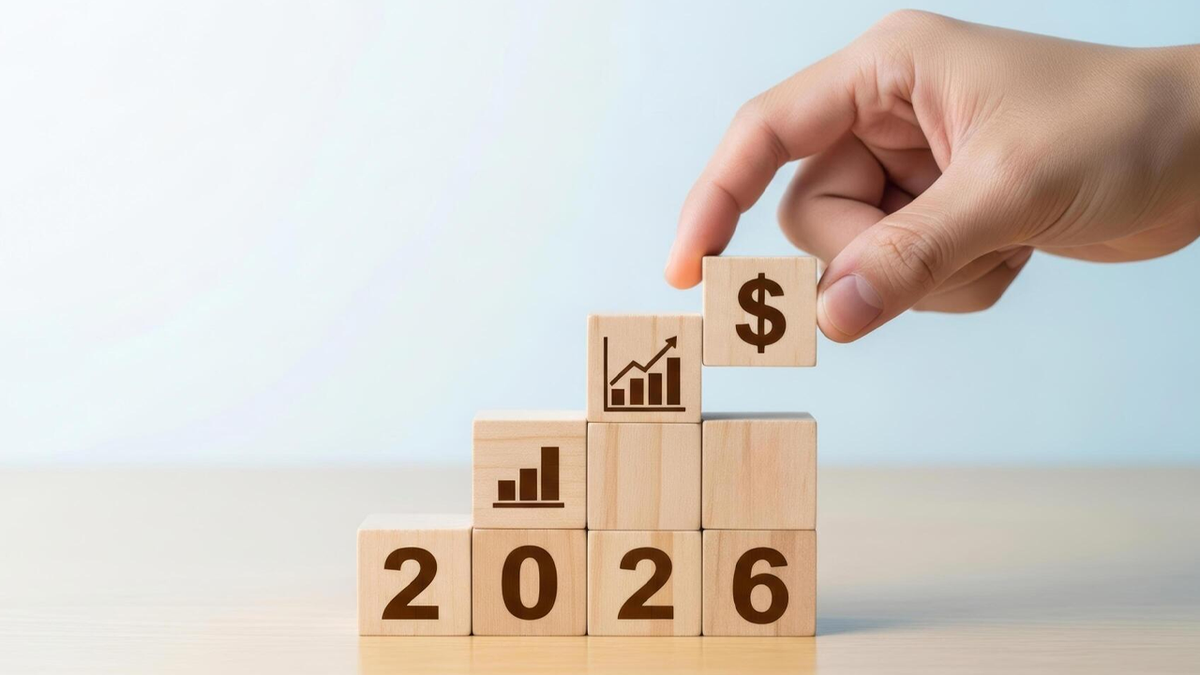 Hand placing a dollar sign block on wooden blocks with '2026' and growth charts.