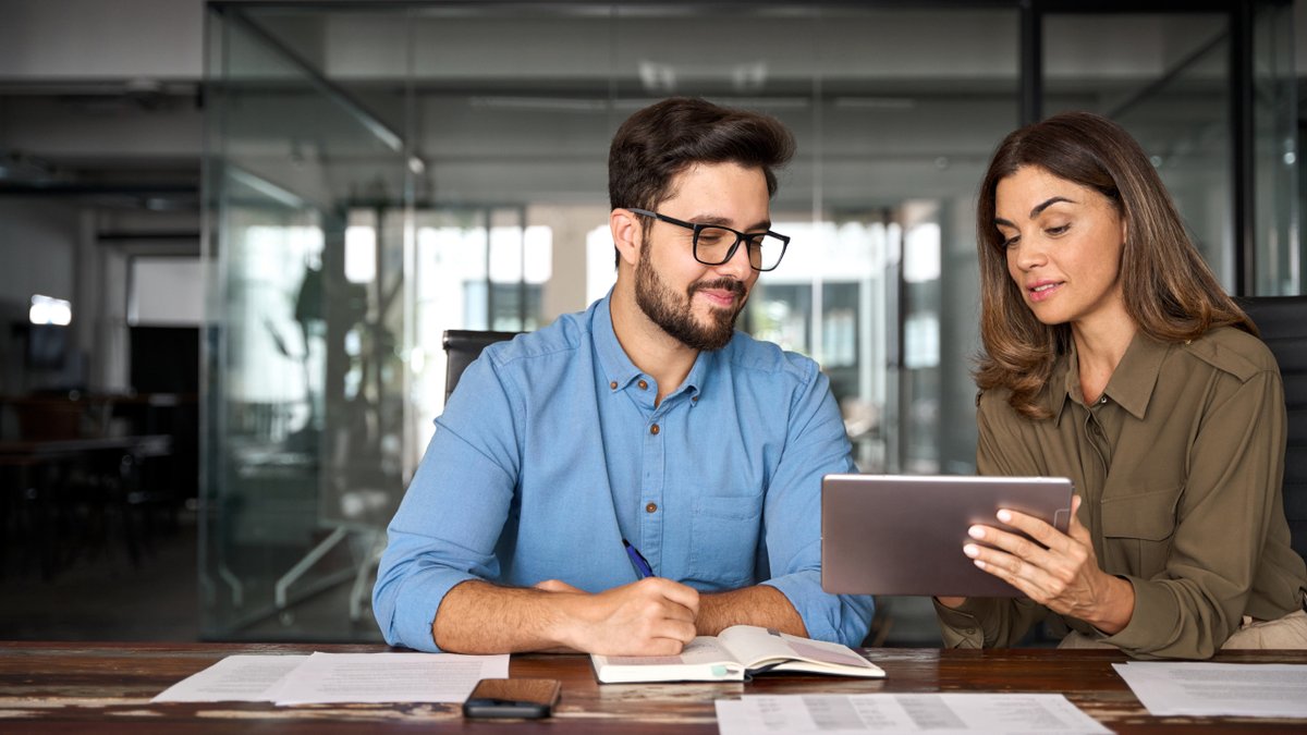 Two colleagues reviewing a tablet and taking notes.