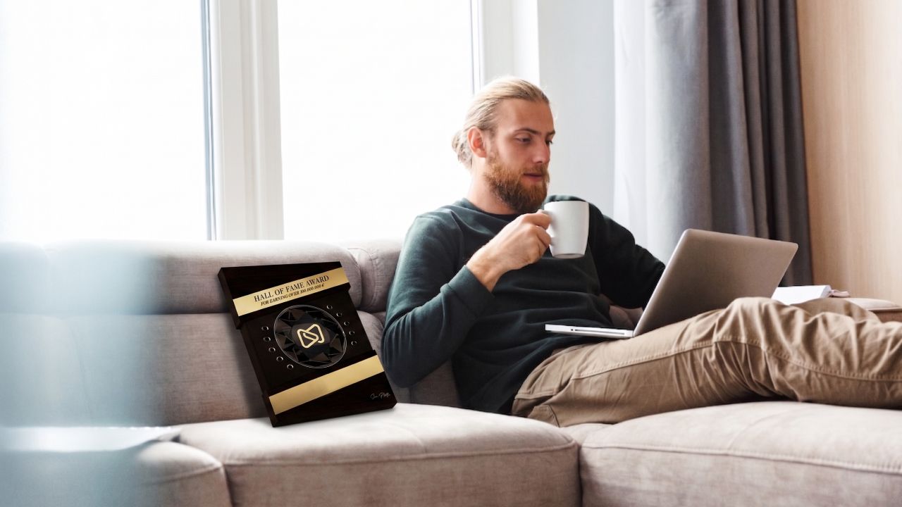Man on a couch with a laptop and coffee mug, next to a black and gold "SEAL OF EXCELLENCE" box.