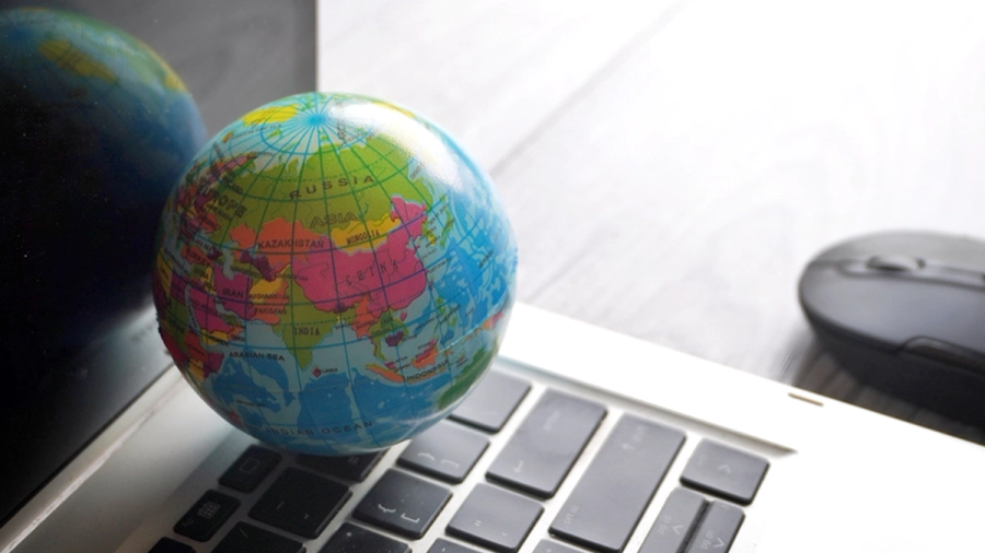 A colorful globe rests on a laptop keyboard, with a computer mouse in the background.