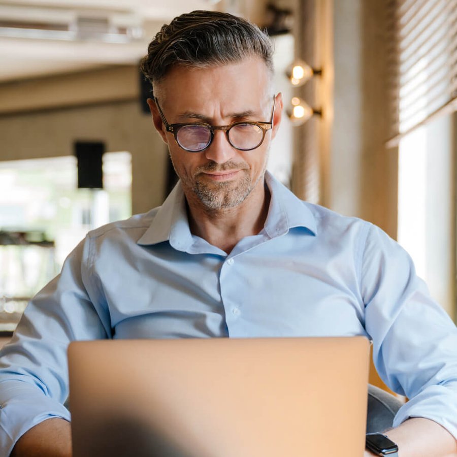 A focused man with glasses and a blue shirt looks at a laptop.