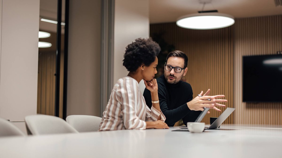 A man and a woman discussing at a conference table with a laptop.