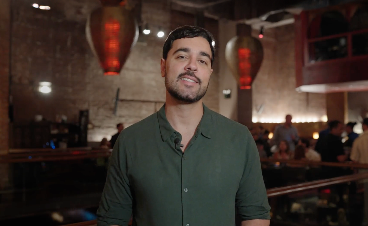 Man in a dark green shirt speaking in a dimly lit restaurant.