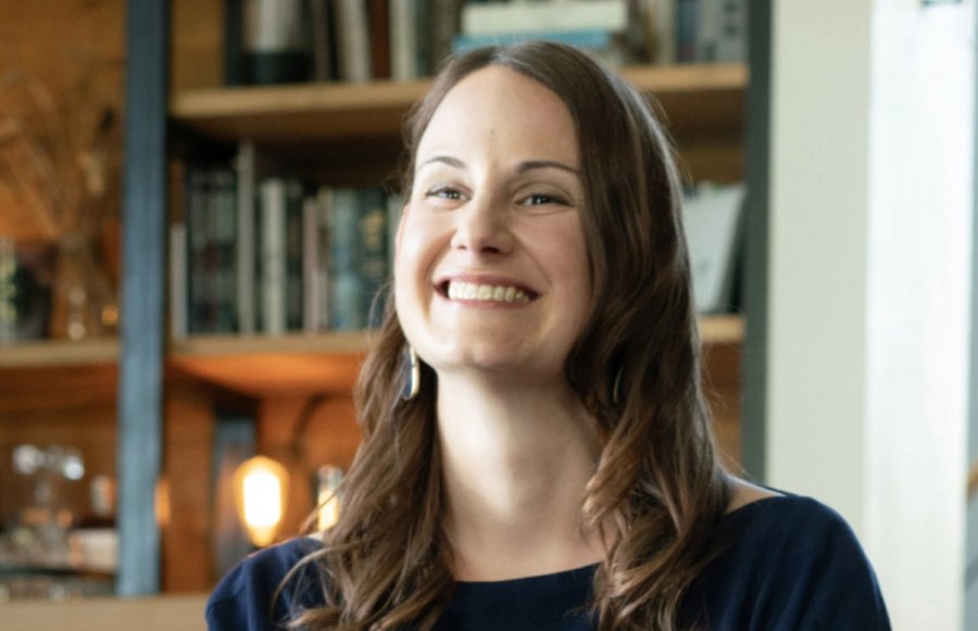 A smiling woman with long brown hair in front of a bookshelf.