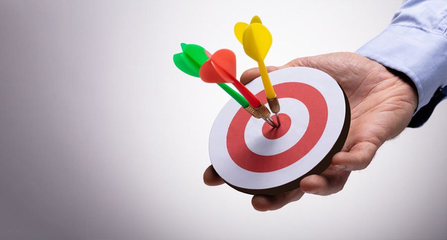 A hand holds a small dartboard with three darts accurately hitting the bullseye.