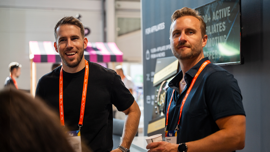 Two men with lanyards at an indoor event, one smiling.