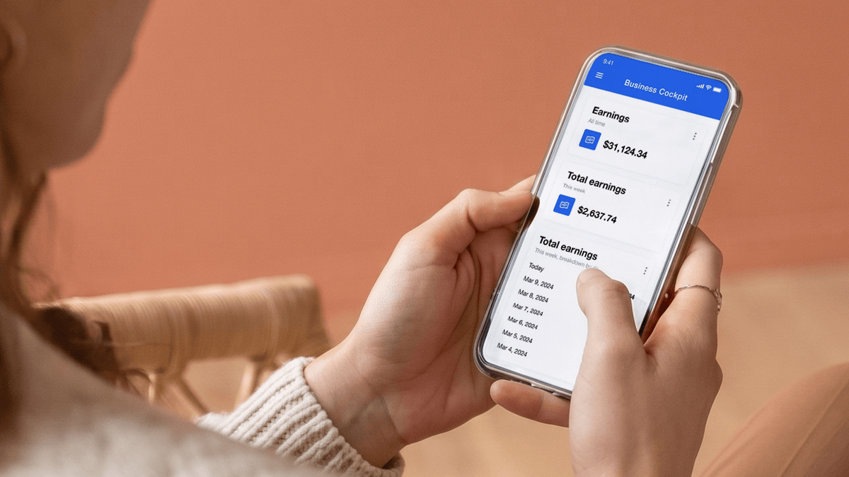 A person's hands hold a smartphone displaying a business earnings app.