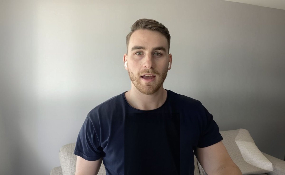 Young man with a beard, dark blue shirt, and white earbuds speaking to the camera.