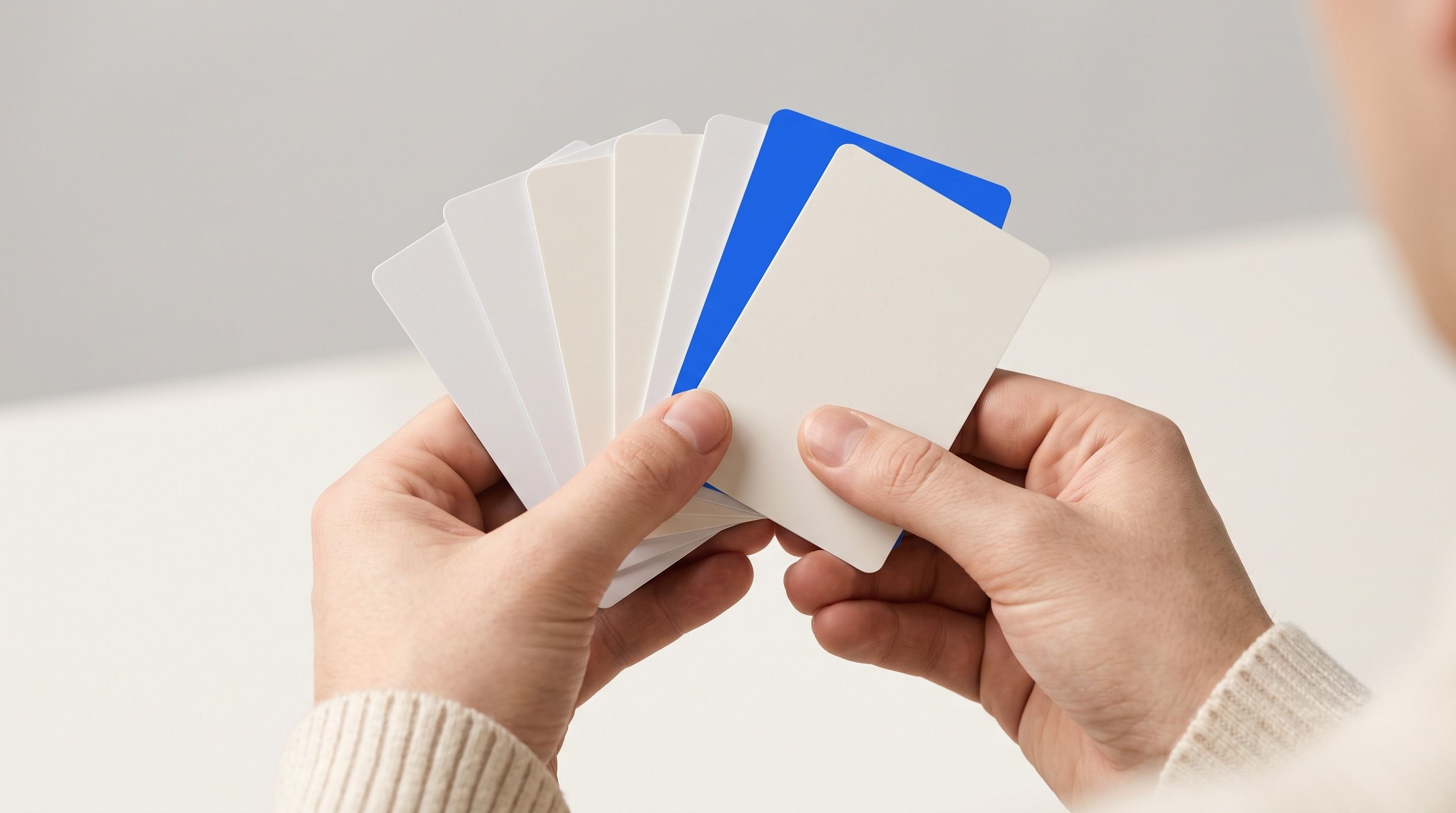 Hands holding a fan of blank cards, including one blue card.