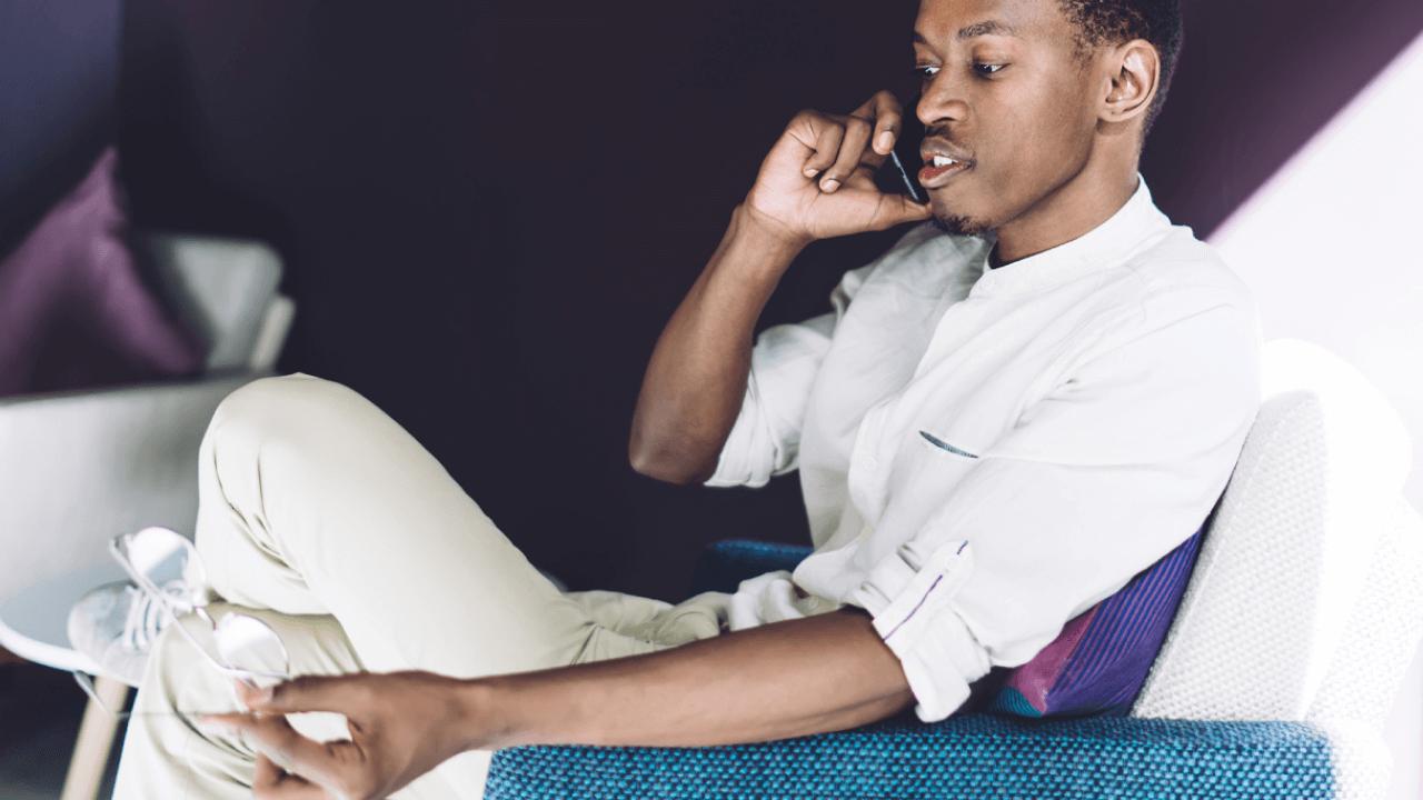 Young Black man talking on a phone and holding eyeglasses.