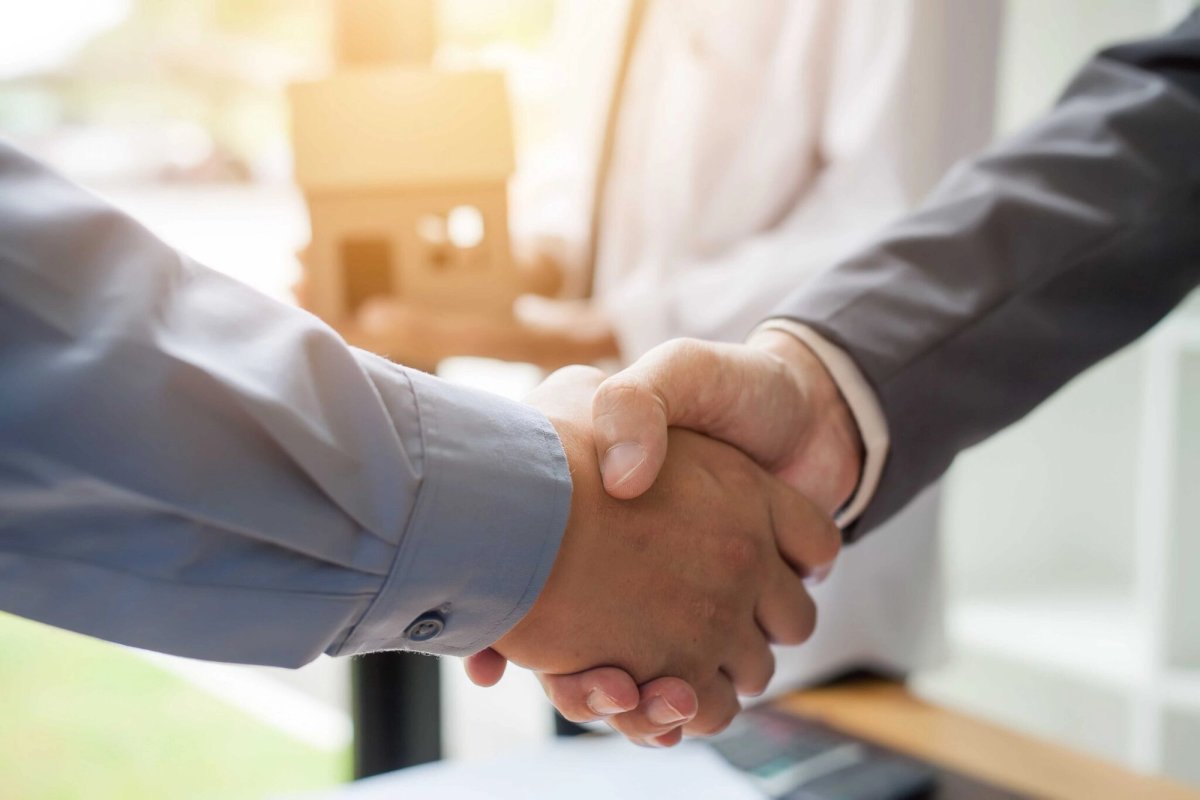 Two people shaking hands with a house model in the background.