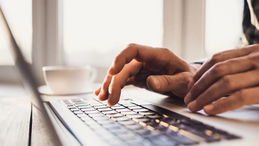 Hands typing on a laptop keyboard with a coffee cup nearby.