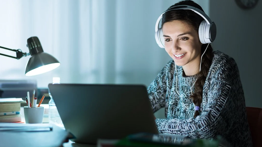 Smiling woman wearing headphones looks at a laptop on a desk.