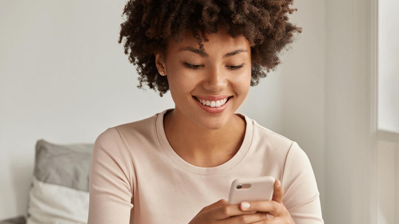 A smiling woman with curly hair looks down at her smartphone.