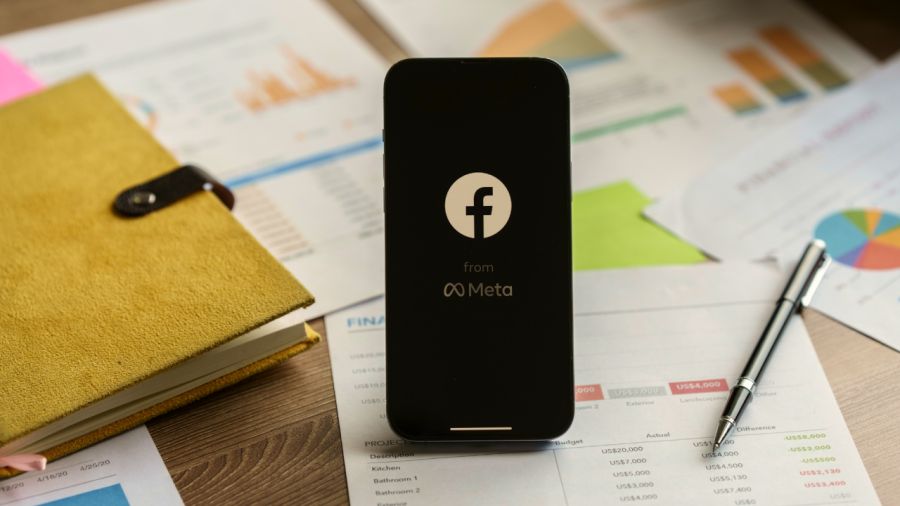 Smartphone displaying Facebook and Meta logos on a desk with financial documents.
