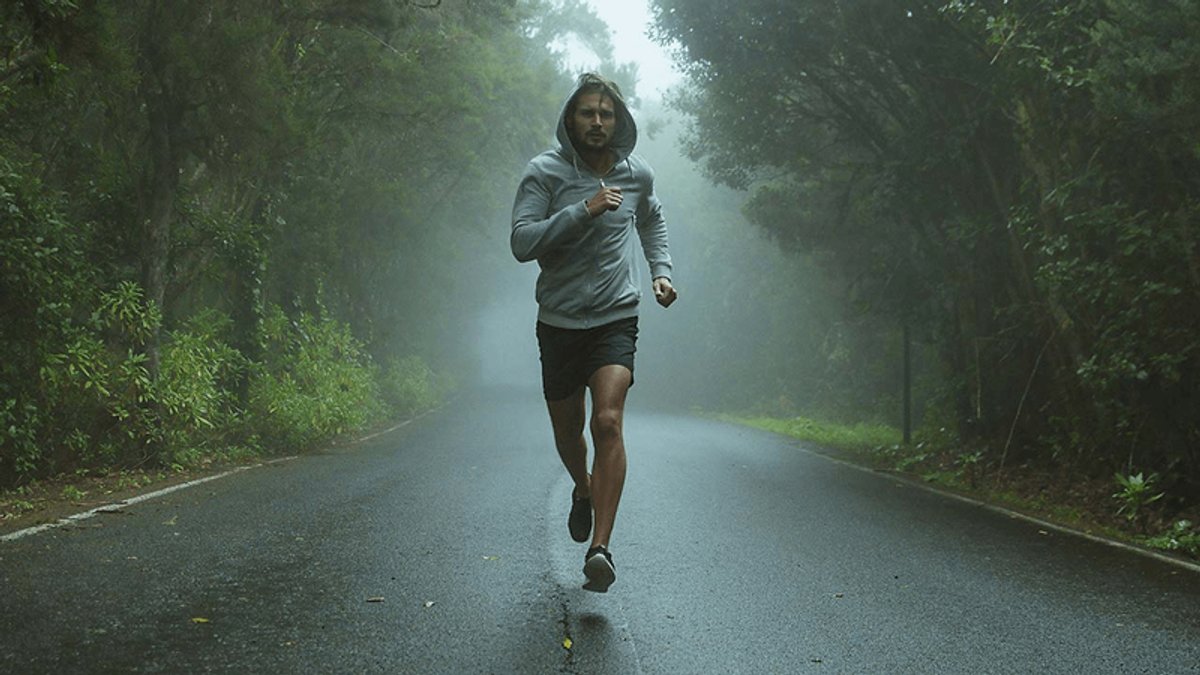A man runs on a misty forest road.