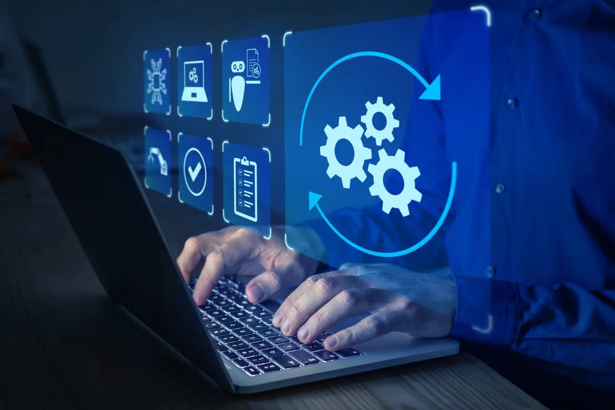 Hands typing on a laptop with a digital overlay showing automation and workflow icons, including a large looping gear symbol.