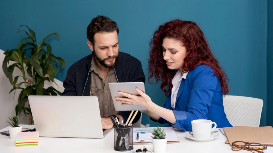 Woman showing a tablet to a man at an office desk.