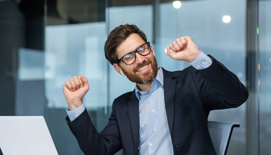 Cheerful businessman with earbuds raising fists in celebration.