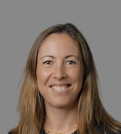 A smiling woman with long light brown hair against a gray background.