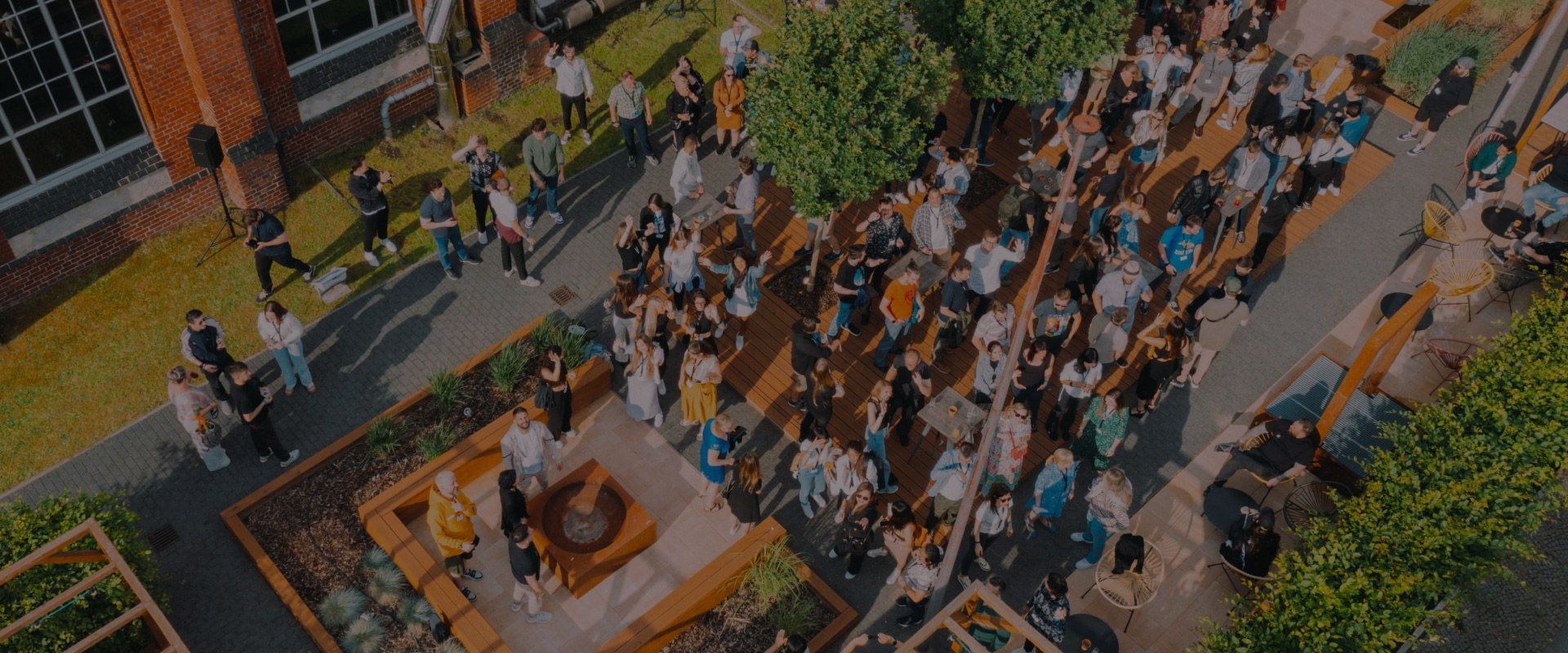 Aerial view of a large group of people gathered in an outdoor courtyard with a brick building and greenery.