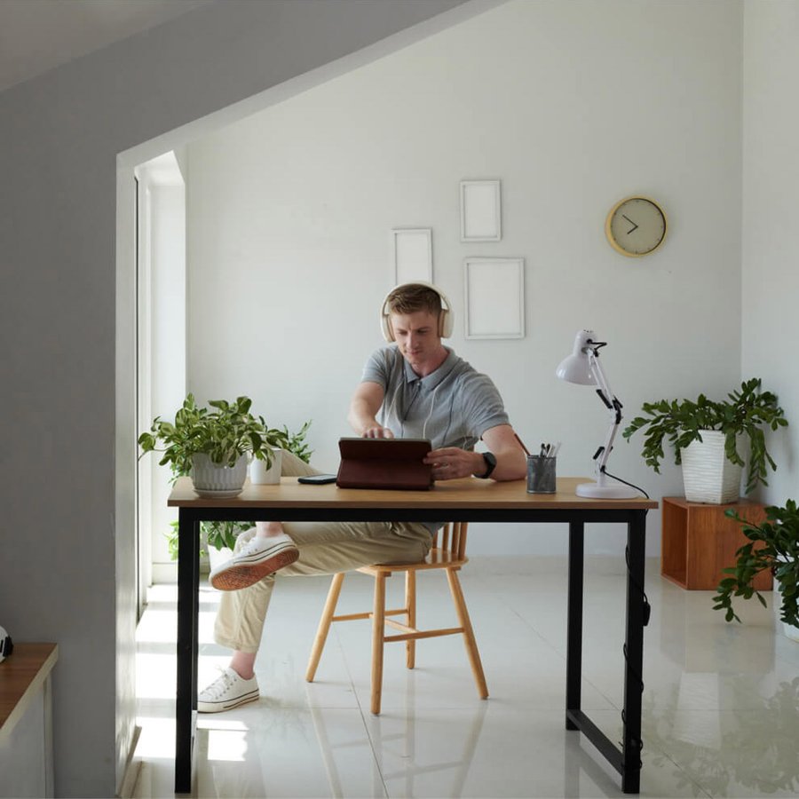 A man in headphones uses a tablet at a desk in a bright room with plants.