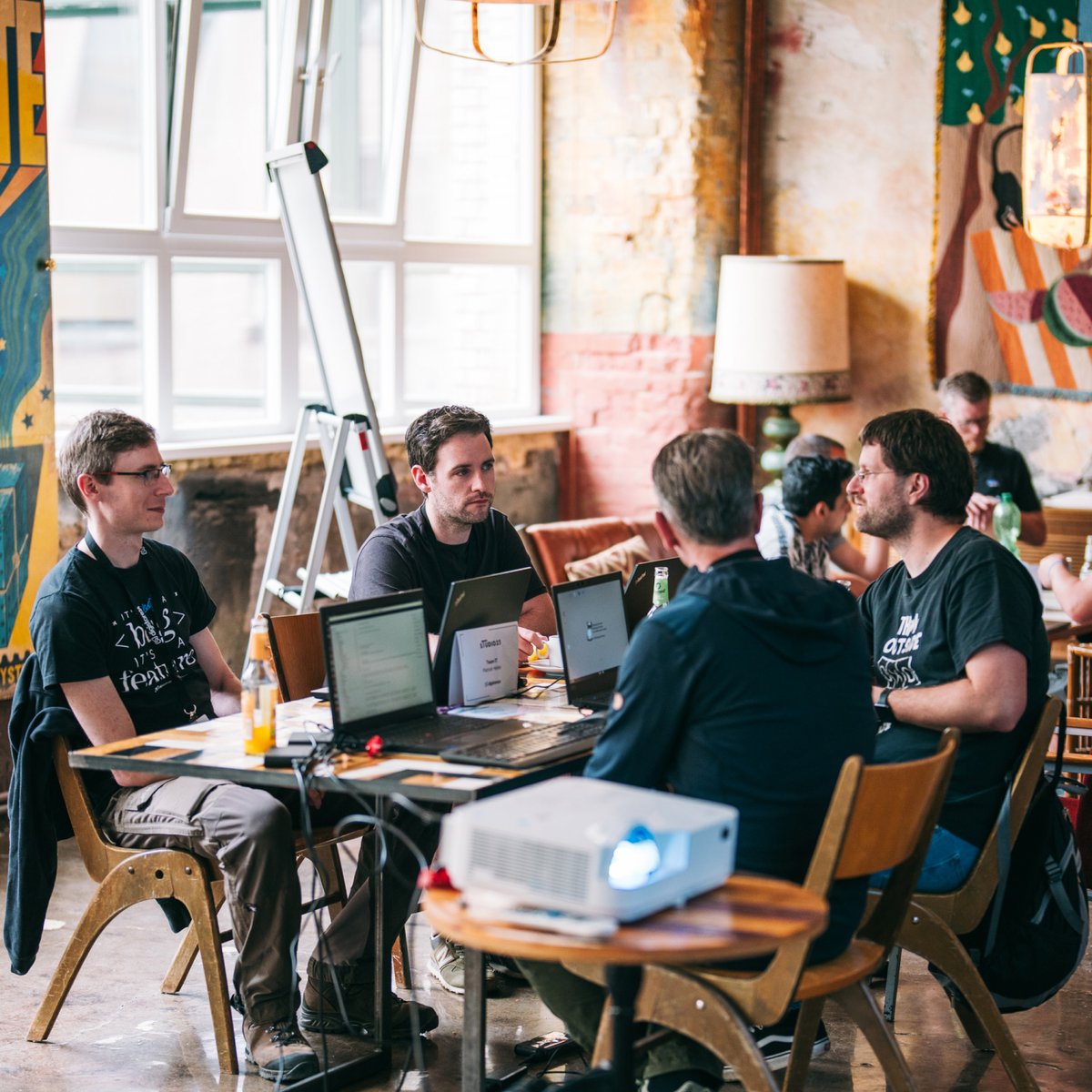 Men collaborating at a table with laptops and a projector in a casual workspace.
