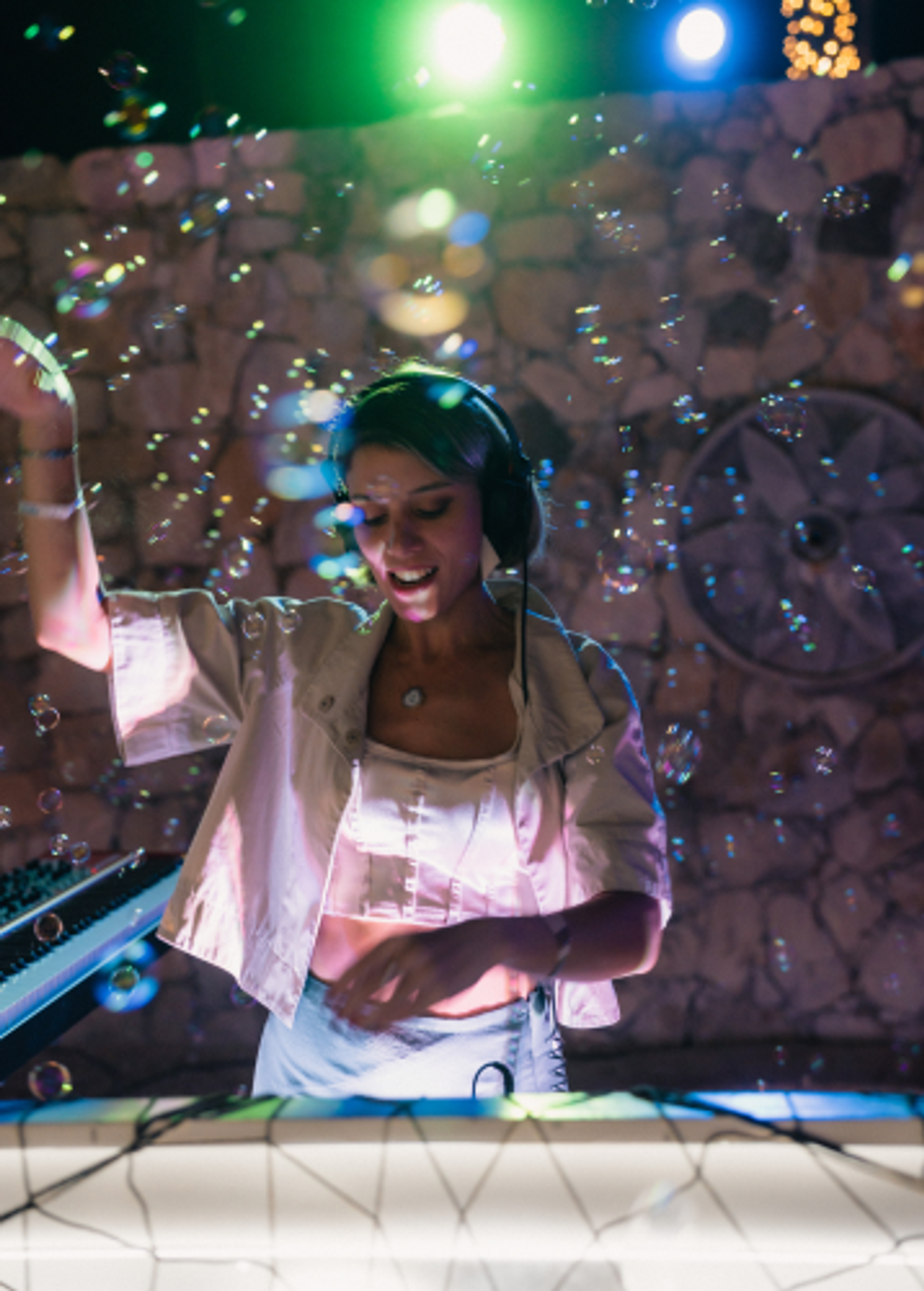 A smiling female DJ with headphones, surrounded by bubbles and colorful lights.