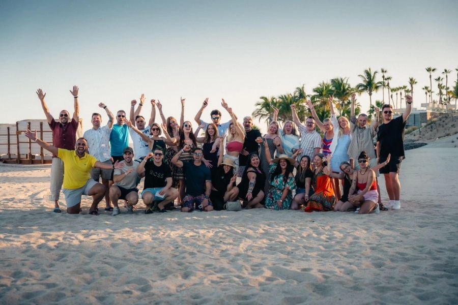 Approximately 30 people celebrating on a tropical beach with raised arms.