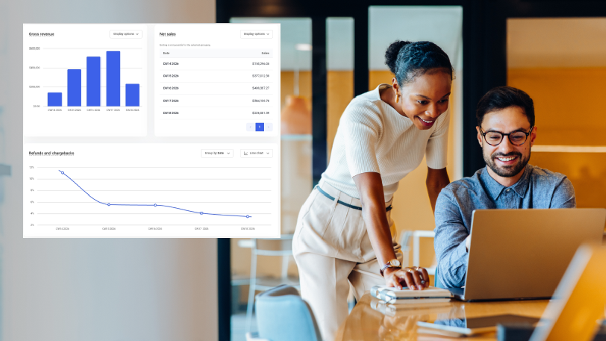Two smiling colleagues review business data on a laptop, with charts for gross revenue, net sales, and refunds displayed.