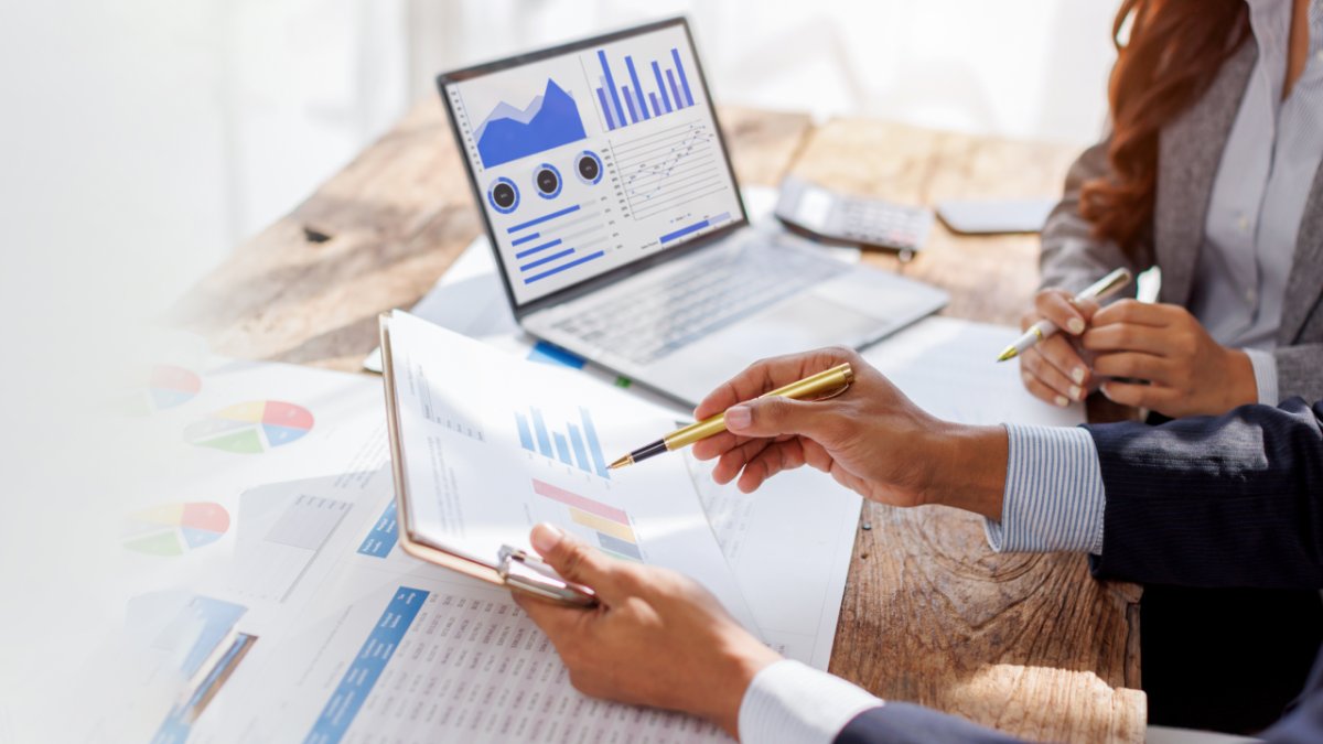 Two professionals analyzing reports and charts on a desk with a laptop.