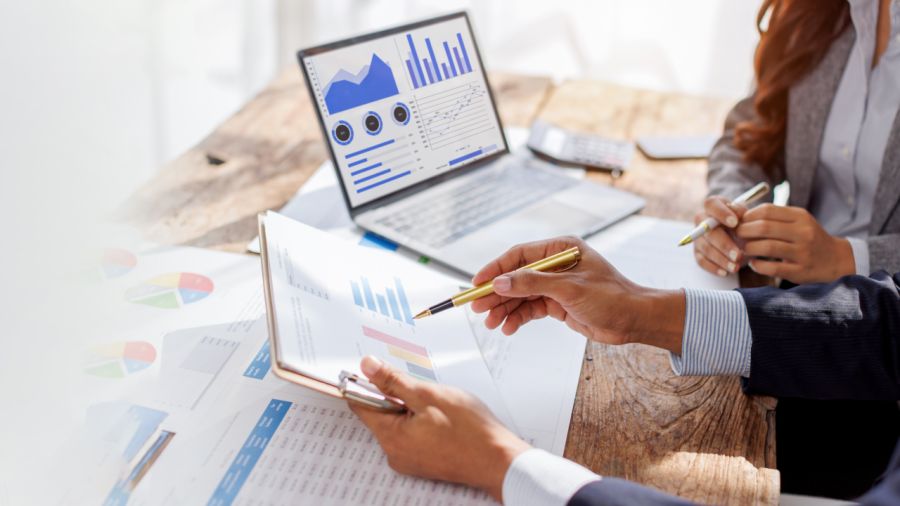 Two professionals analyzing reports and charts on a desk with a laptop.