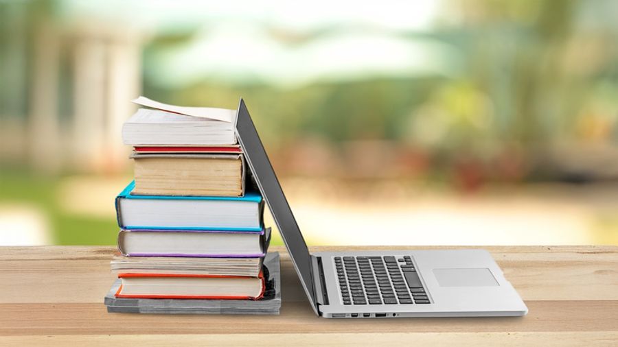 A stack of books next to an open laptop on a wooden desk.